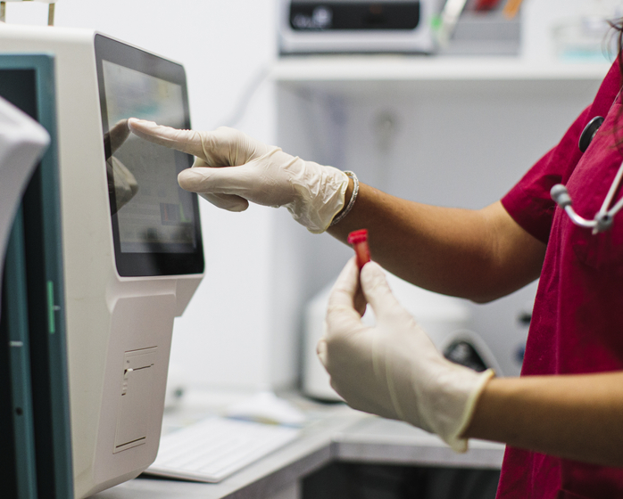 A closeup of a medical professional holding a blood sample and using a touch screen on medical equipment.