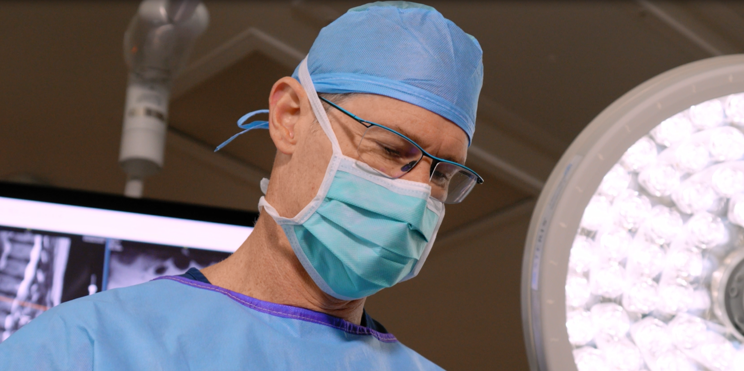 Yoav Ritter in front of surgical light performing surgery.