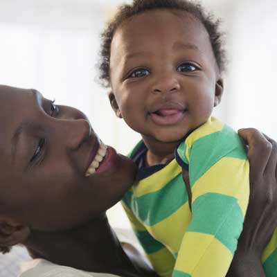 A woman smiles at her infant while holding him up in the air.