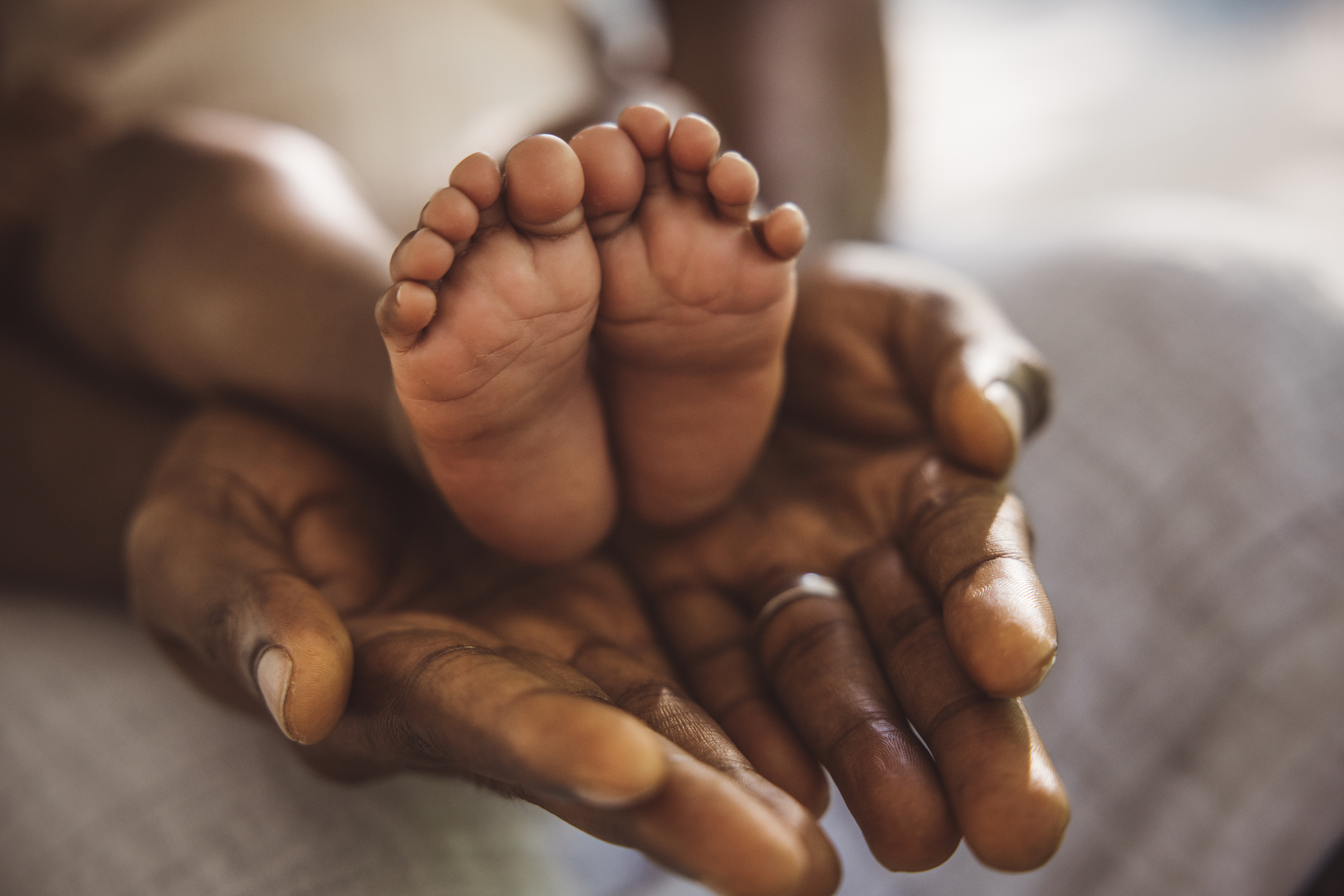 Adult hands gently cradling small infant feet in their hands.