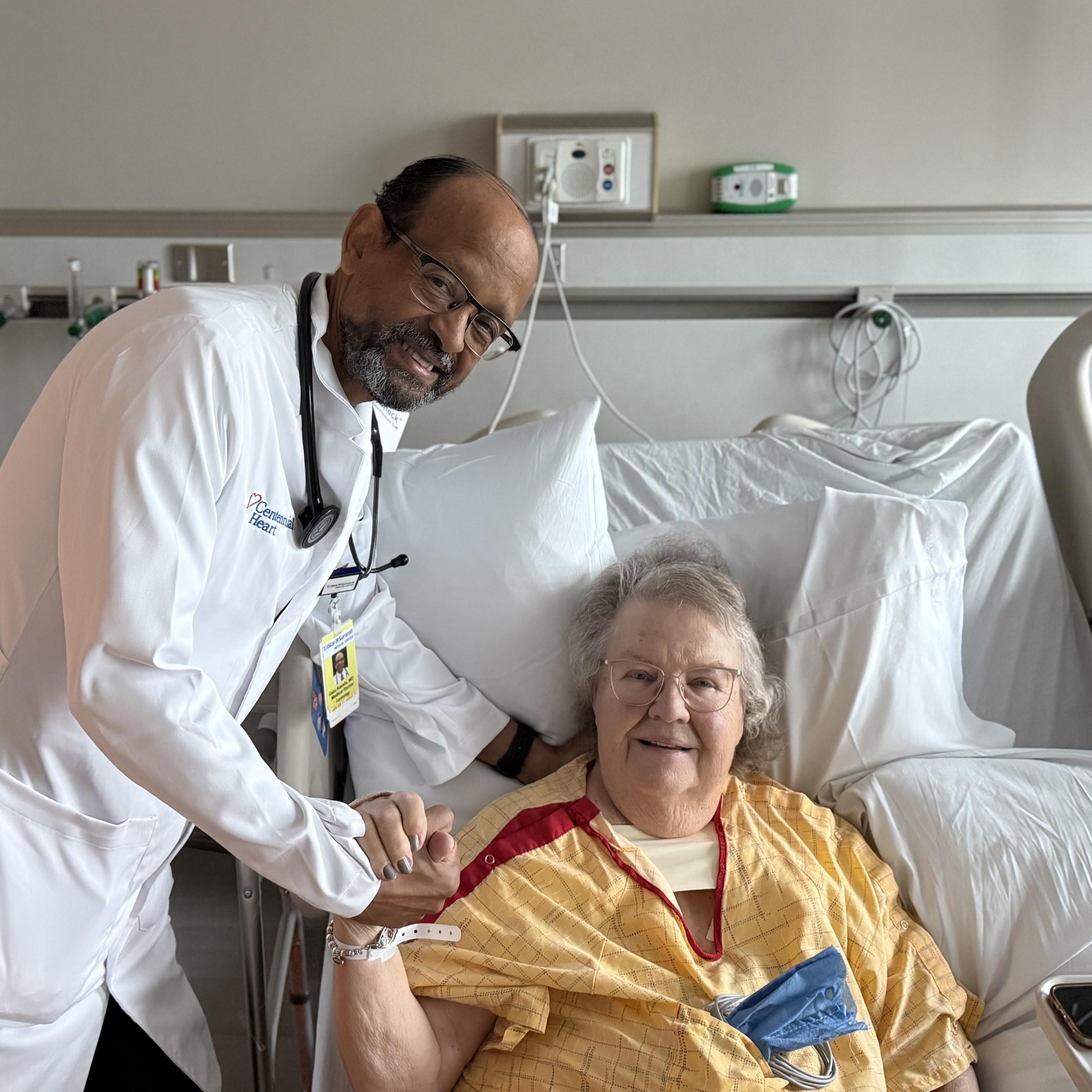 Carol Kraemer smiling in hospital bed holding hands with Dr. Getu Assefa.