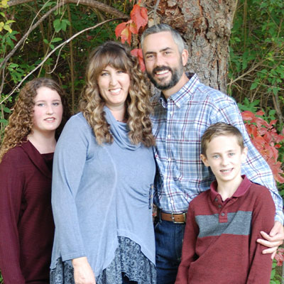 Laraine smiles and poses with her husband and children in outdoor-themed photo studio.