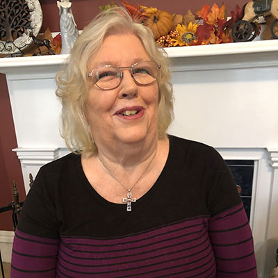 Mary Routh smiles while sitting in front of her fireplace.