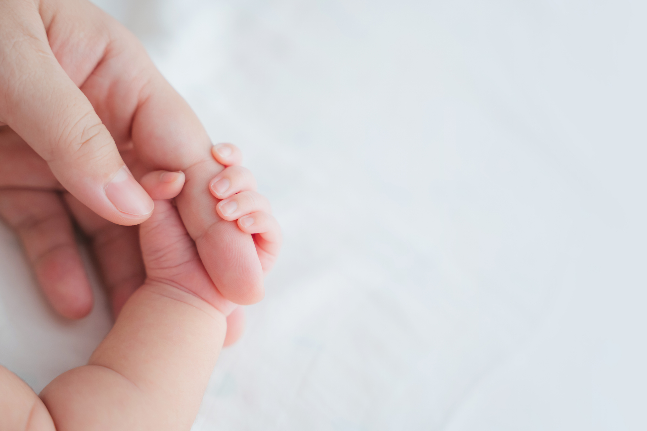 Newborn baby hand holding onto an adult woman's finger