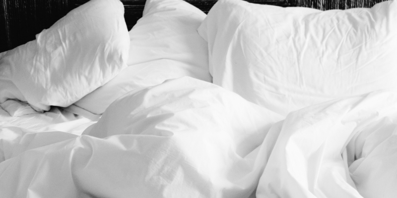 An unmade bed of white blankets and pillows.