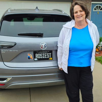 Woman standing beside a gray SUV in a driveway, smiling at the camera.