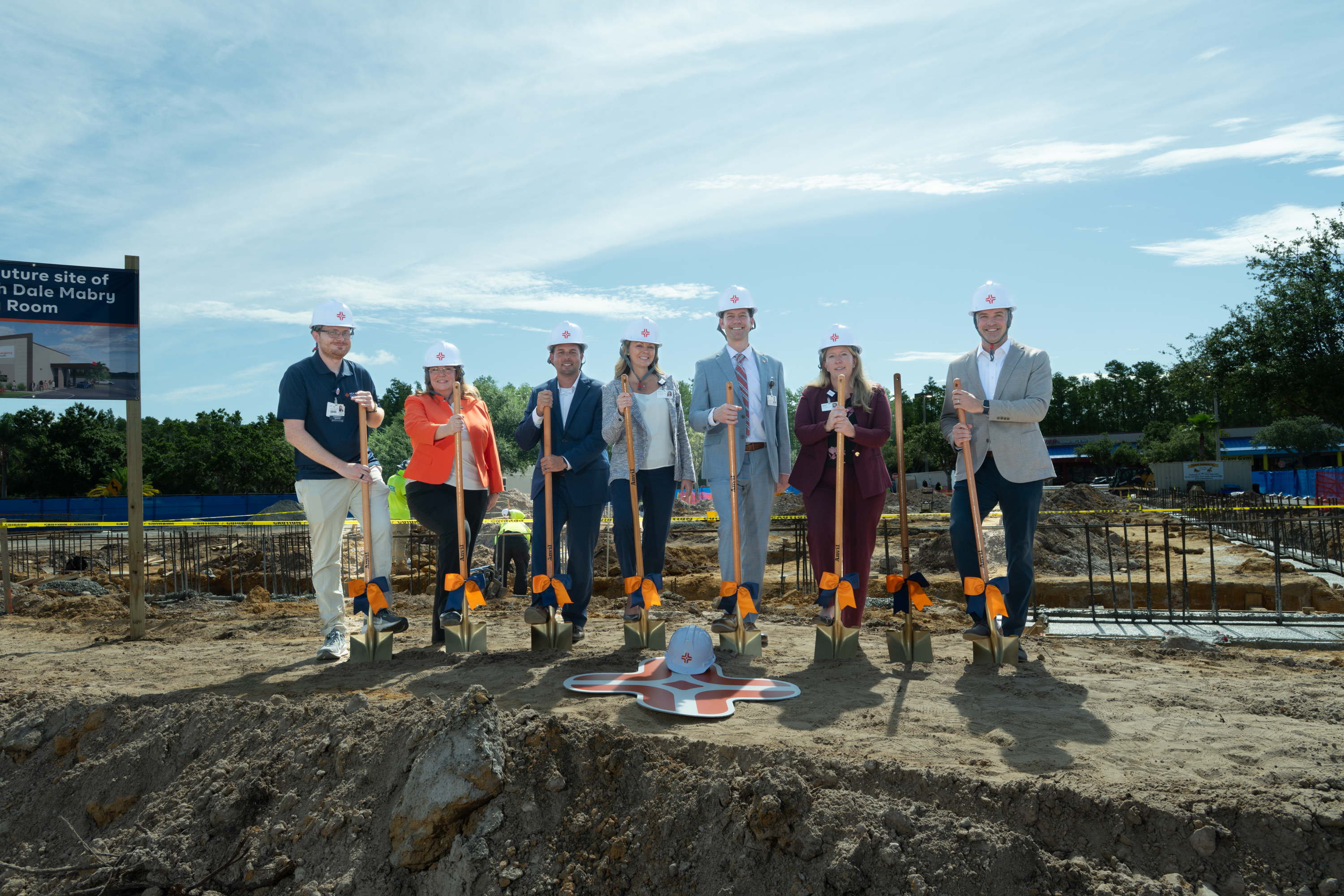 HCA representatives in hard hats and shovels break ceremonial ground at new construction site.