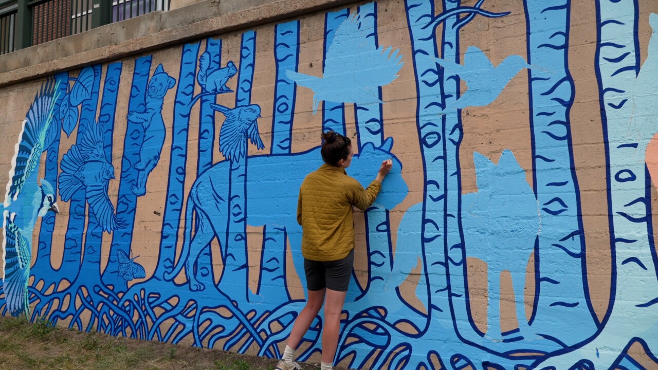 A person painting a large jungle cat in blue paint on a wall outside