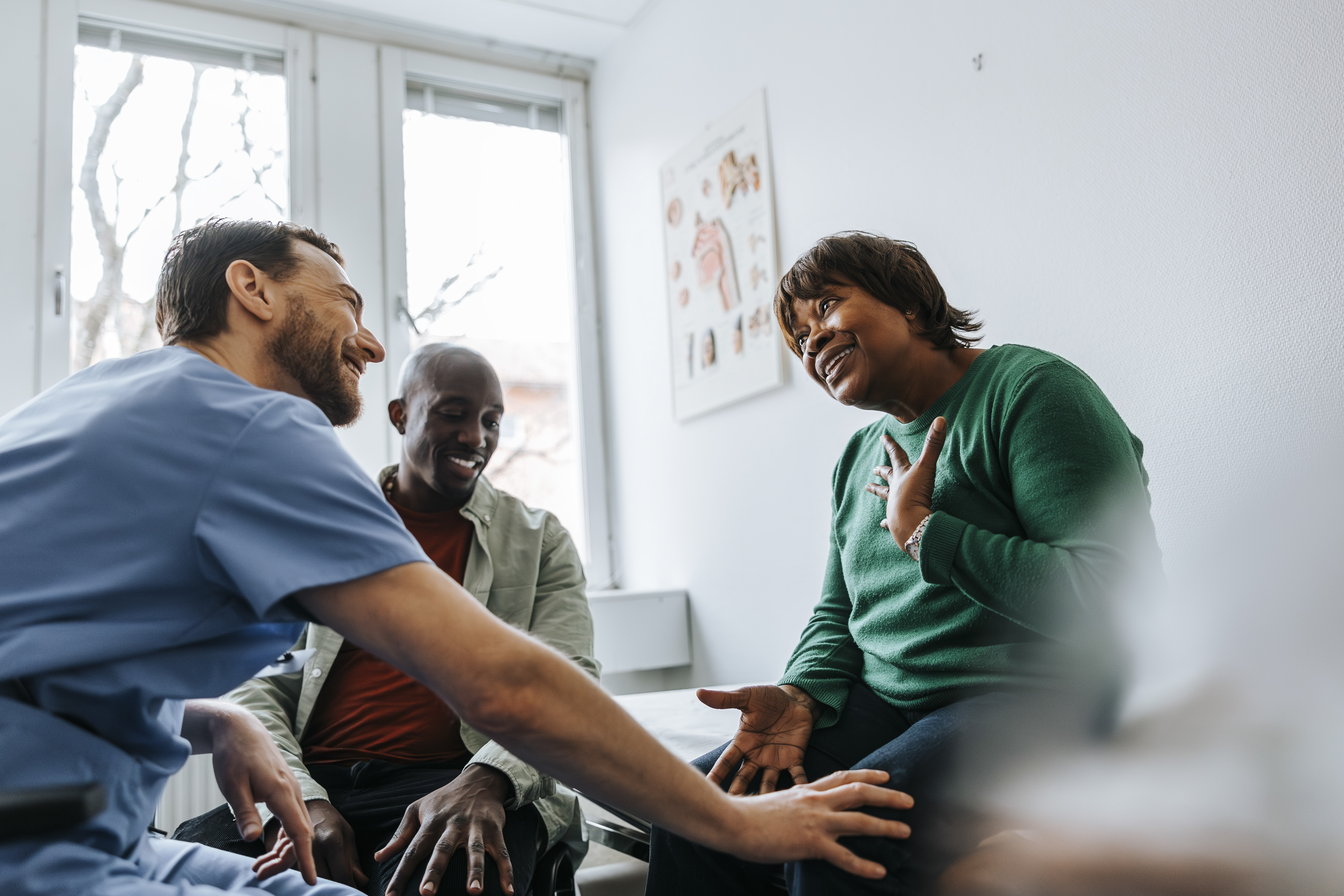 Healthcare worker chatting with a senior patient and her son in an examination room.