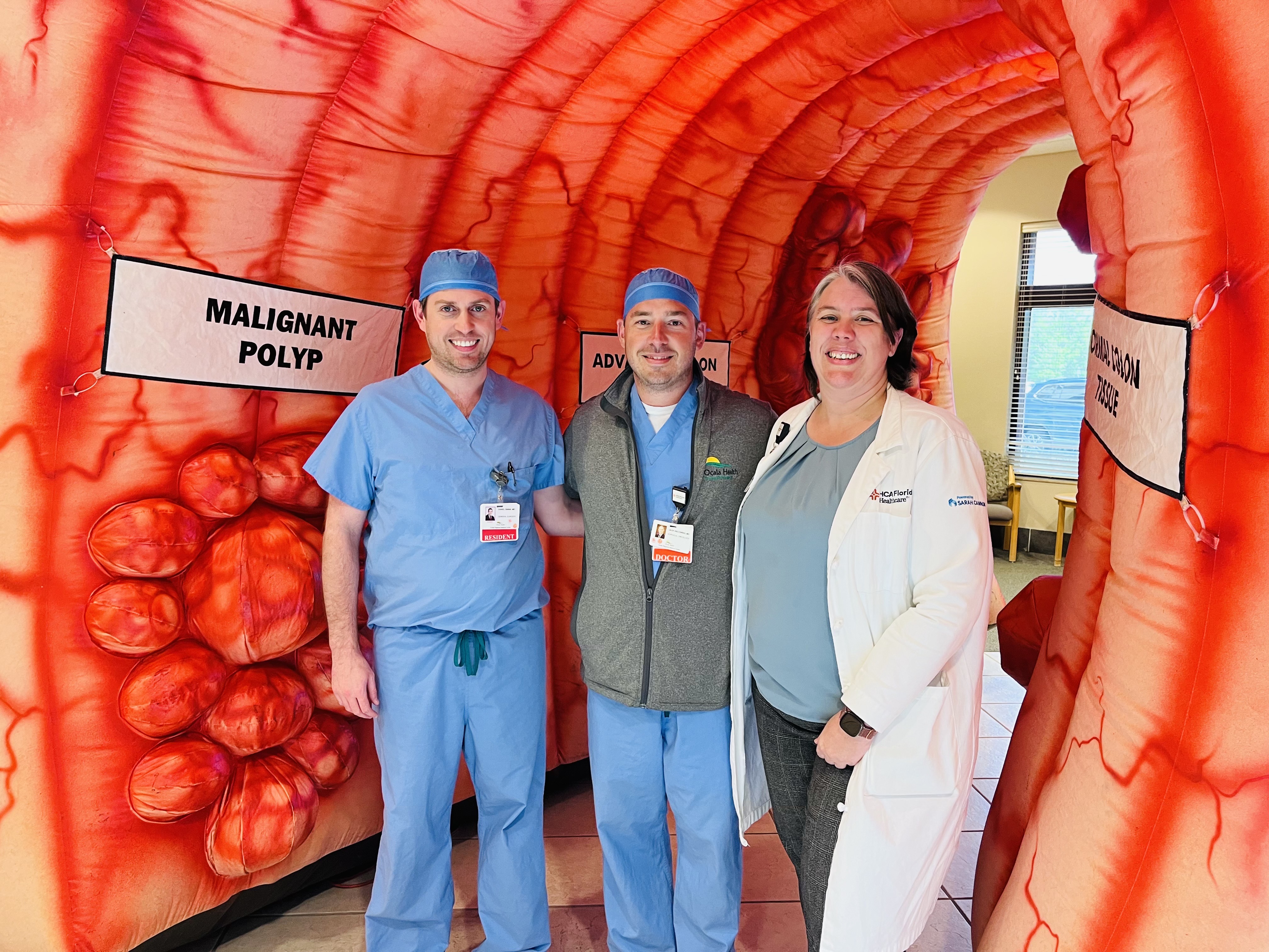 Photo shows Dr. Weckowski and two team members standing in an education tunnel shaped like a colon.