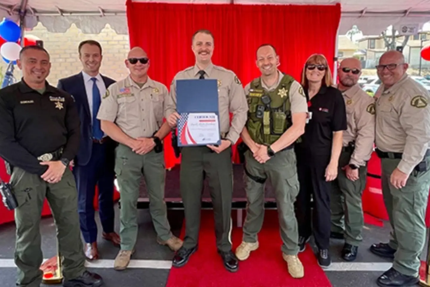 Deputy Oldenburg smiles with a group of officers and medical professionals, holding a certificate honoring his service for saving a life.