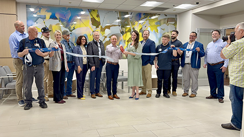 A group of hospital staff smile for a picture while holding a ceremonial ribbon during the new opening of the hospital facilities.