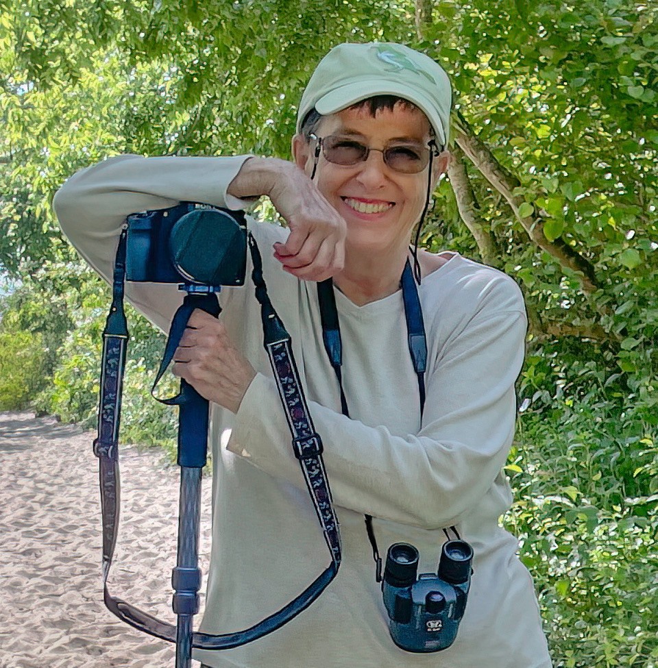 Nancy Goetzinger smiles while standing on a trail  with her camera.