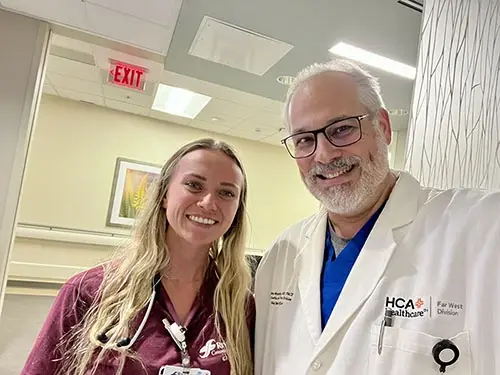 A female nurse and male doctor dressed in physician's jacket and hospital scrubs smiling.