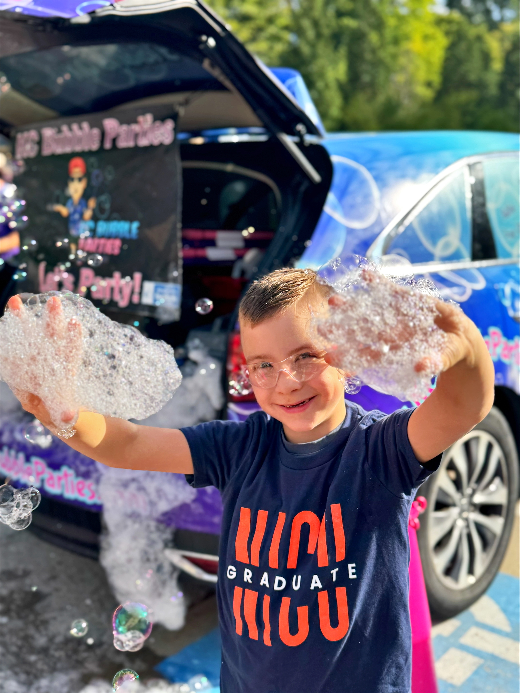 A child with soap bubbles on hands, smiling for the camera, wearing a "NICU Graduate" T-Shirt.