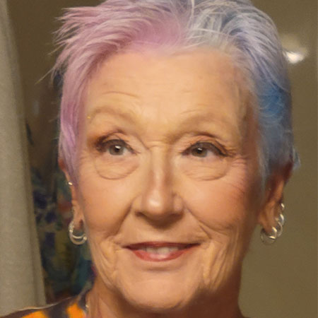 Zona Newell Morgan smiles while wearing gold hoop earrings and her hair is dyed blue and purple.