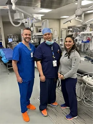 A group of medial staff dressed in hospital scrubs smiles in an operating room.