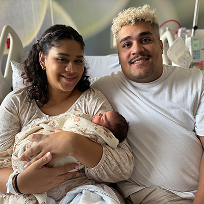 Genevieve and Daniel with their baby sitting together in a hospital bed.