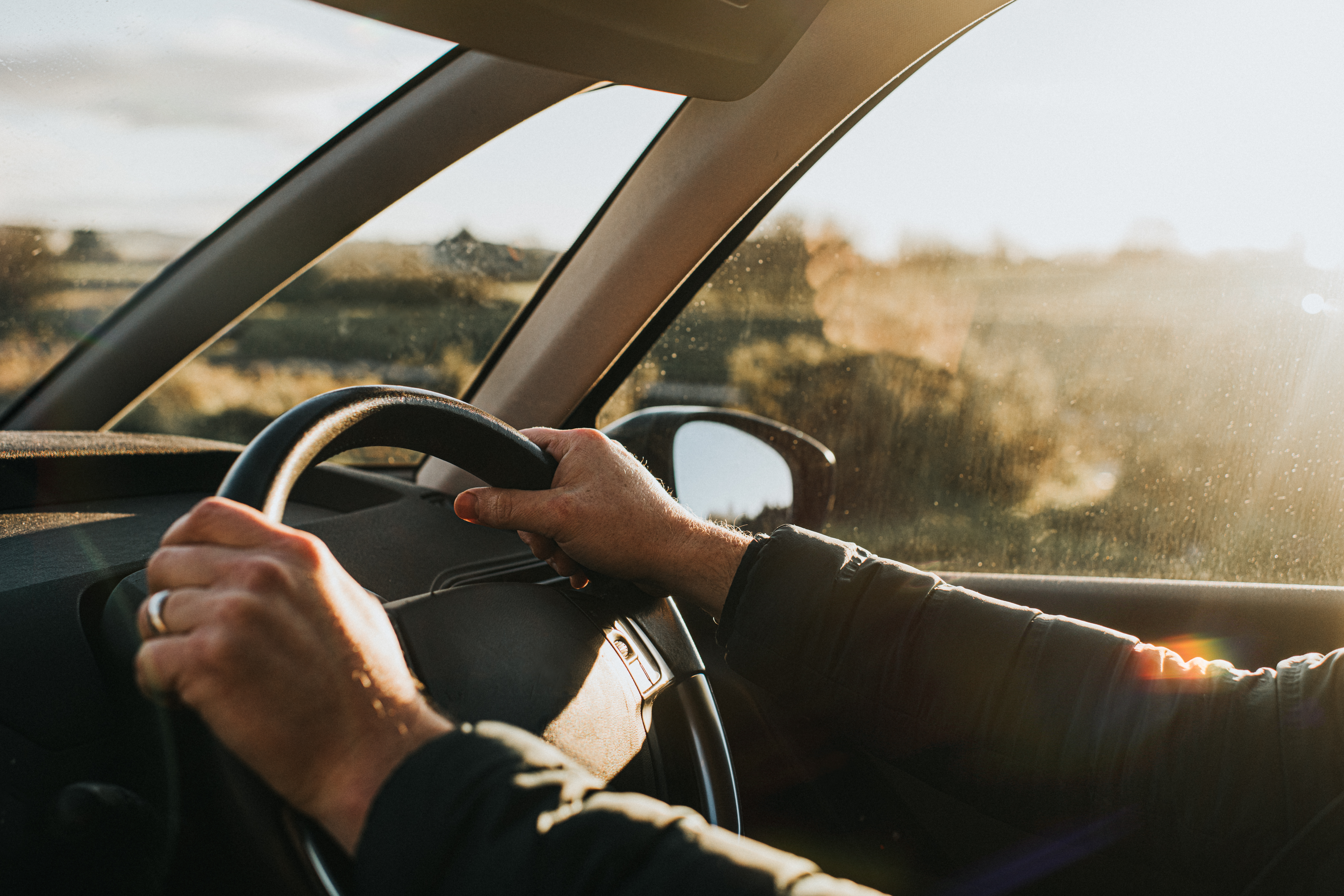 Man with hands on the steering wheel of a vehicle.