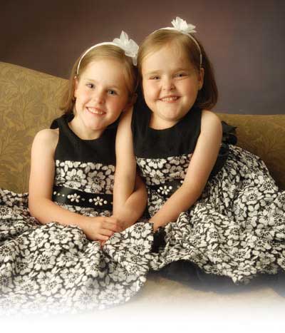 Erin Herrin's twin daughter's, Melea and Kendra, smile while embracing and wearing matching black and white flower print dresses.