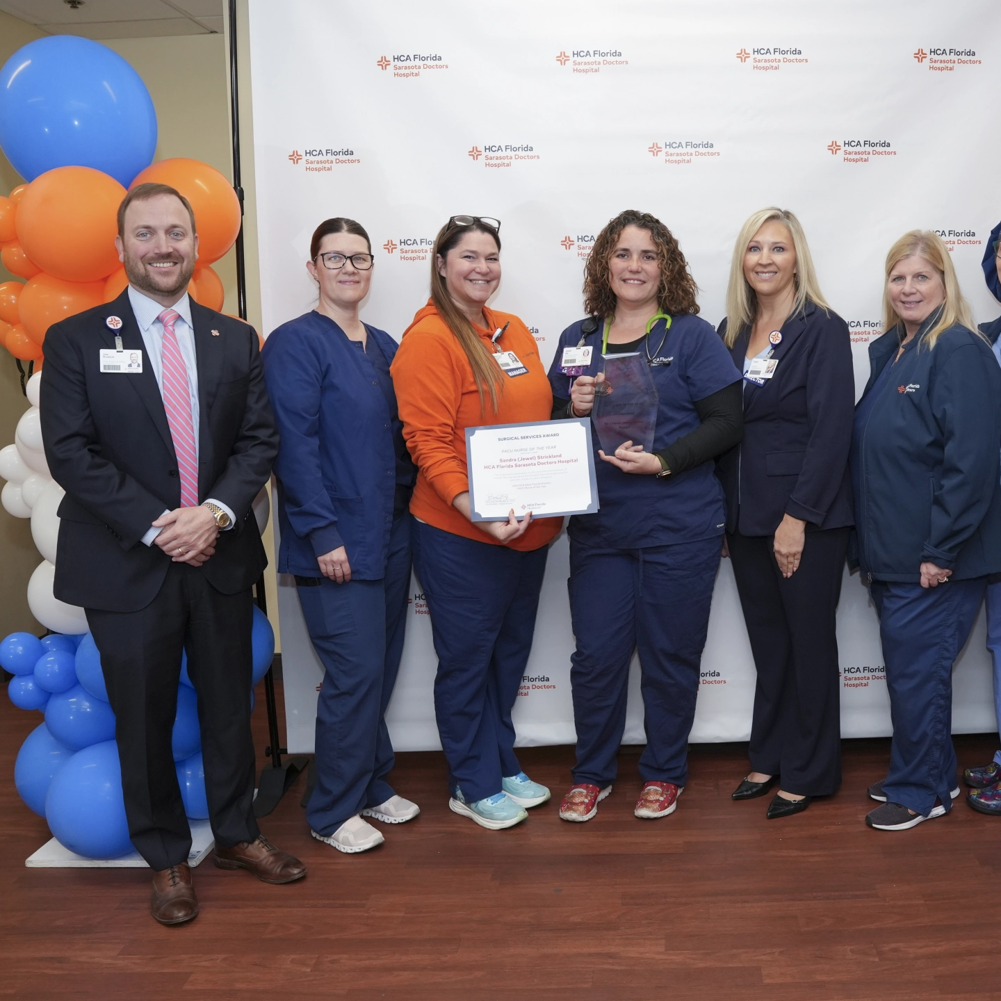 Nurse stands smiling with other nurses holding award