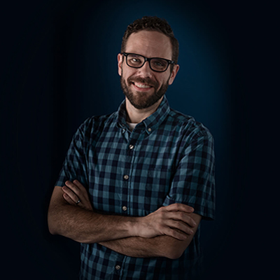 Brian E. smiling with his arms crossed, wearing a checkered shirt.