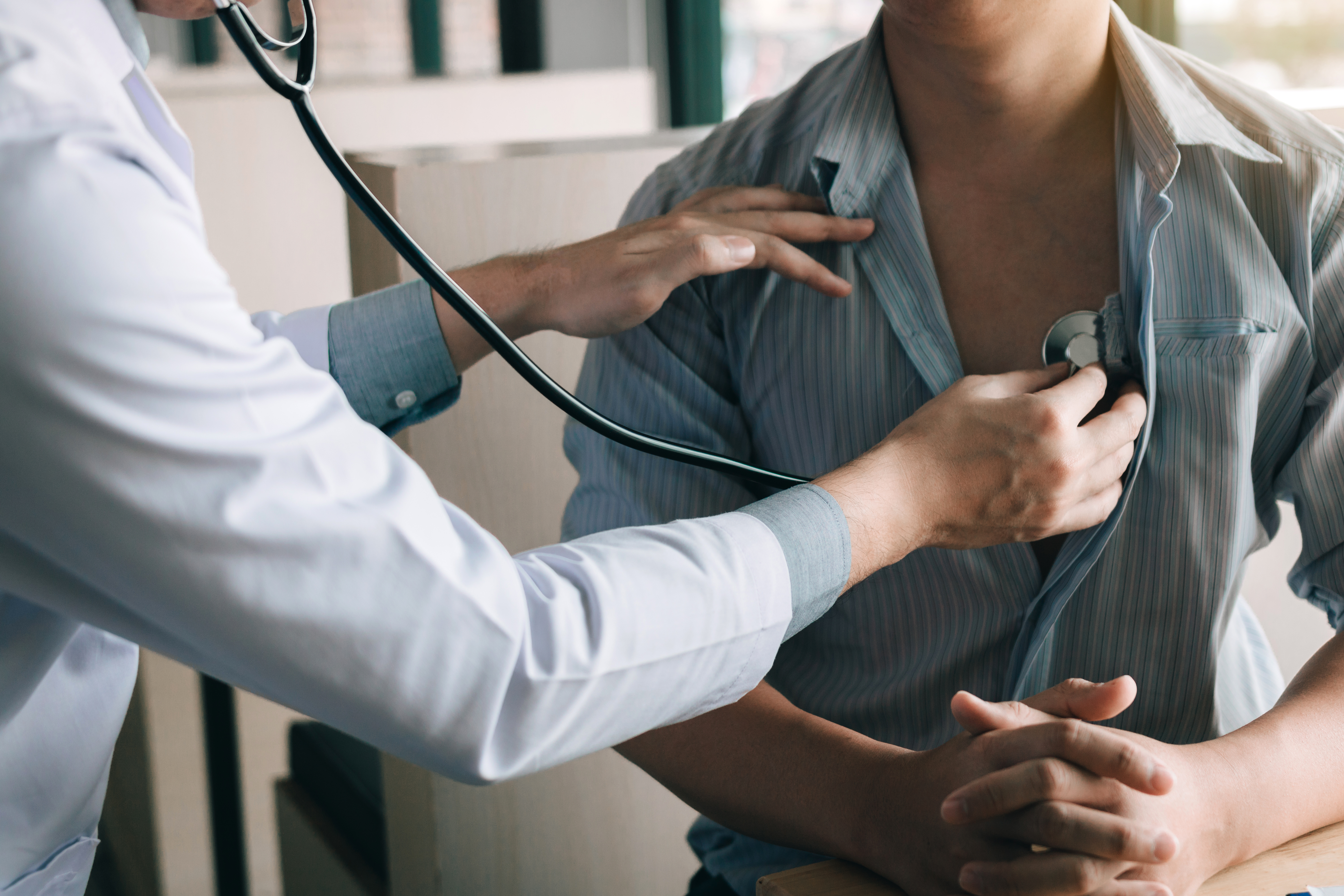 A closeup of a patient with a medical professional listening to their heart through a stethoscope.