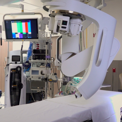 Wide view of an operating room, with a large white robotic arm over a draped table.