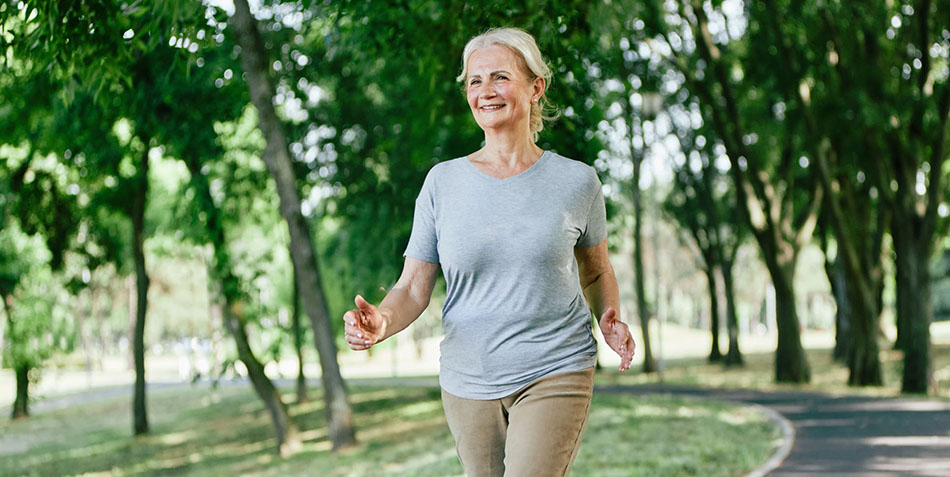 Smiling active senior woman jogging running and walking doing fitness in the park.