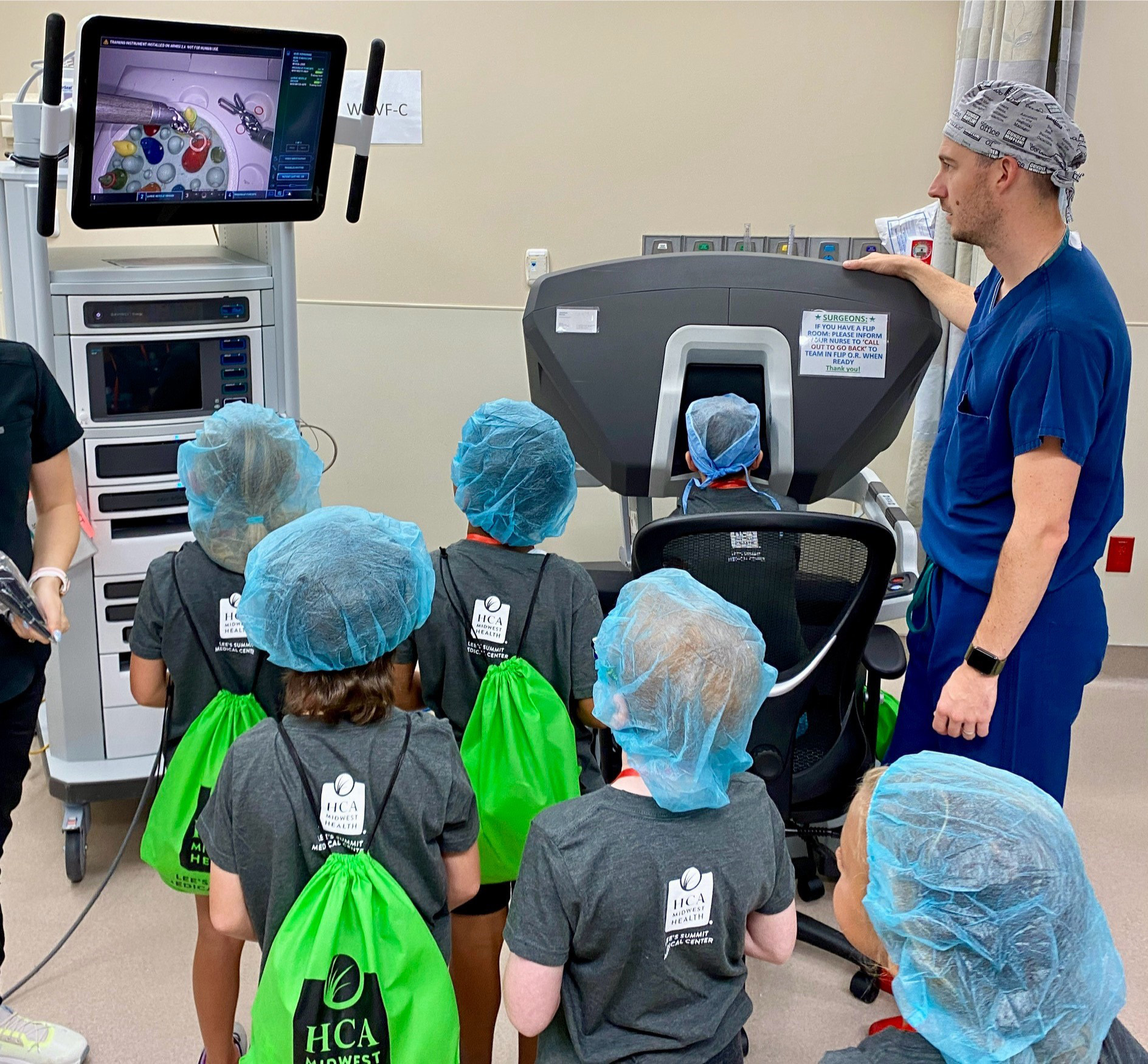 Physician with group of young kids giving demo of medical equipment system.