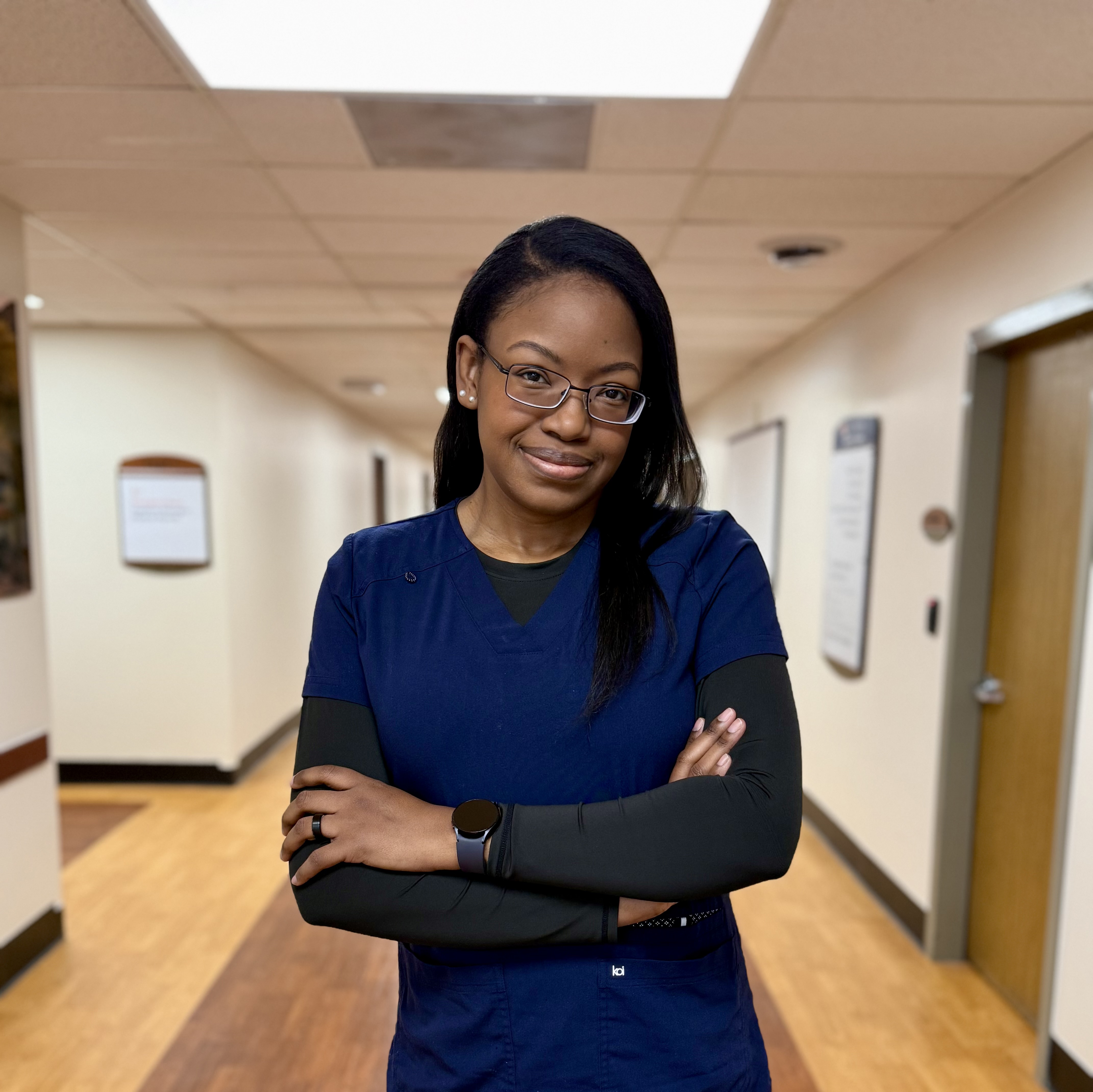 Genevieve Antoine in dark blue scrubs smiling in hospital hallway.