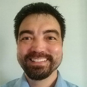 Billy Hunawill smiling and wearing a blue button up shirt.