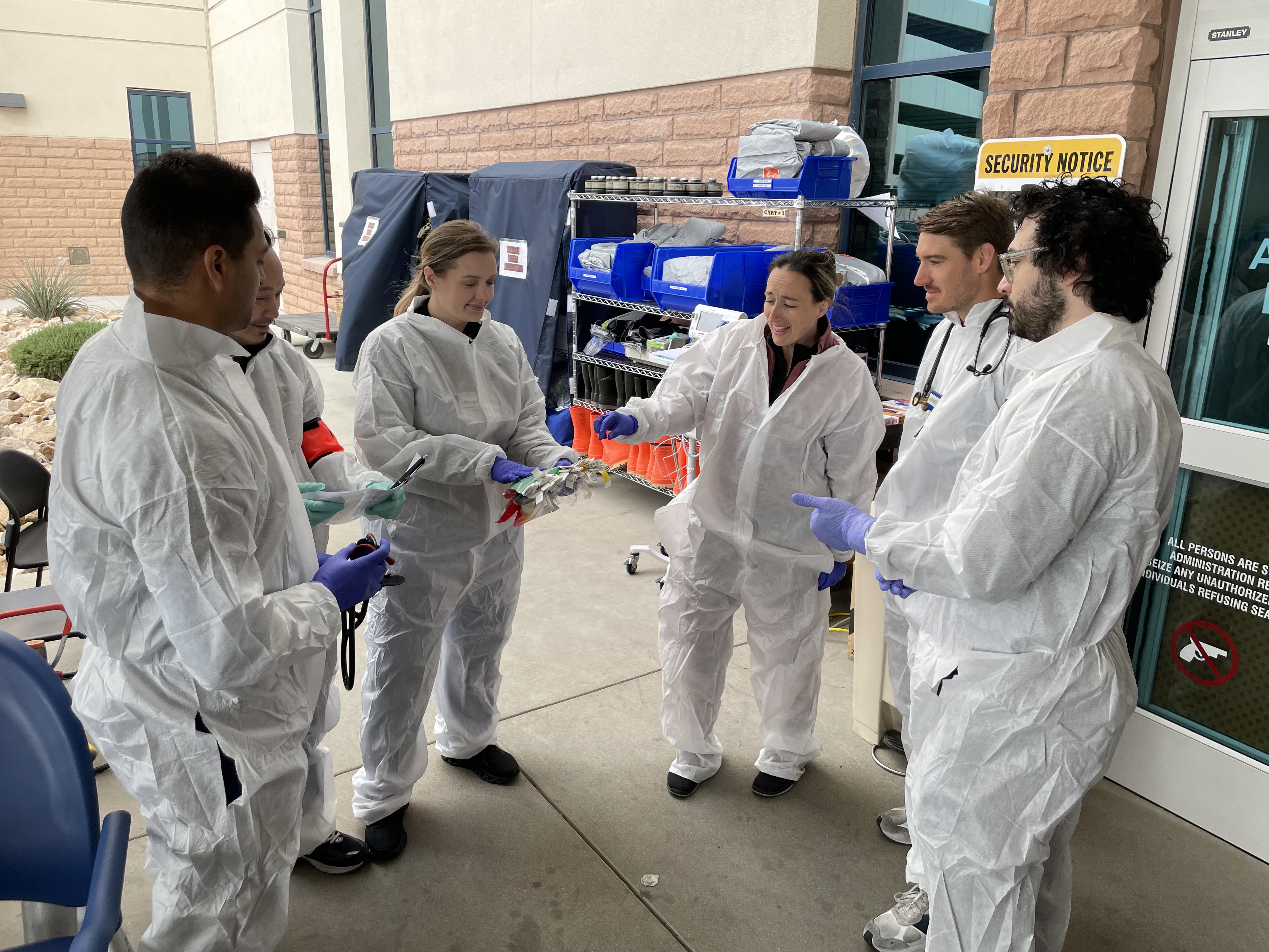 A group of four in hazmat suits gather outside the hospital.