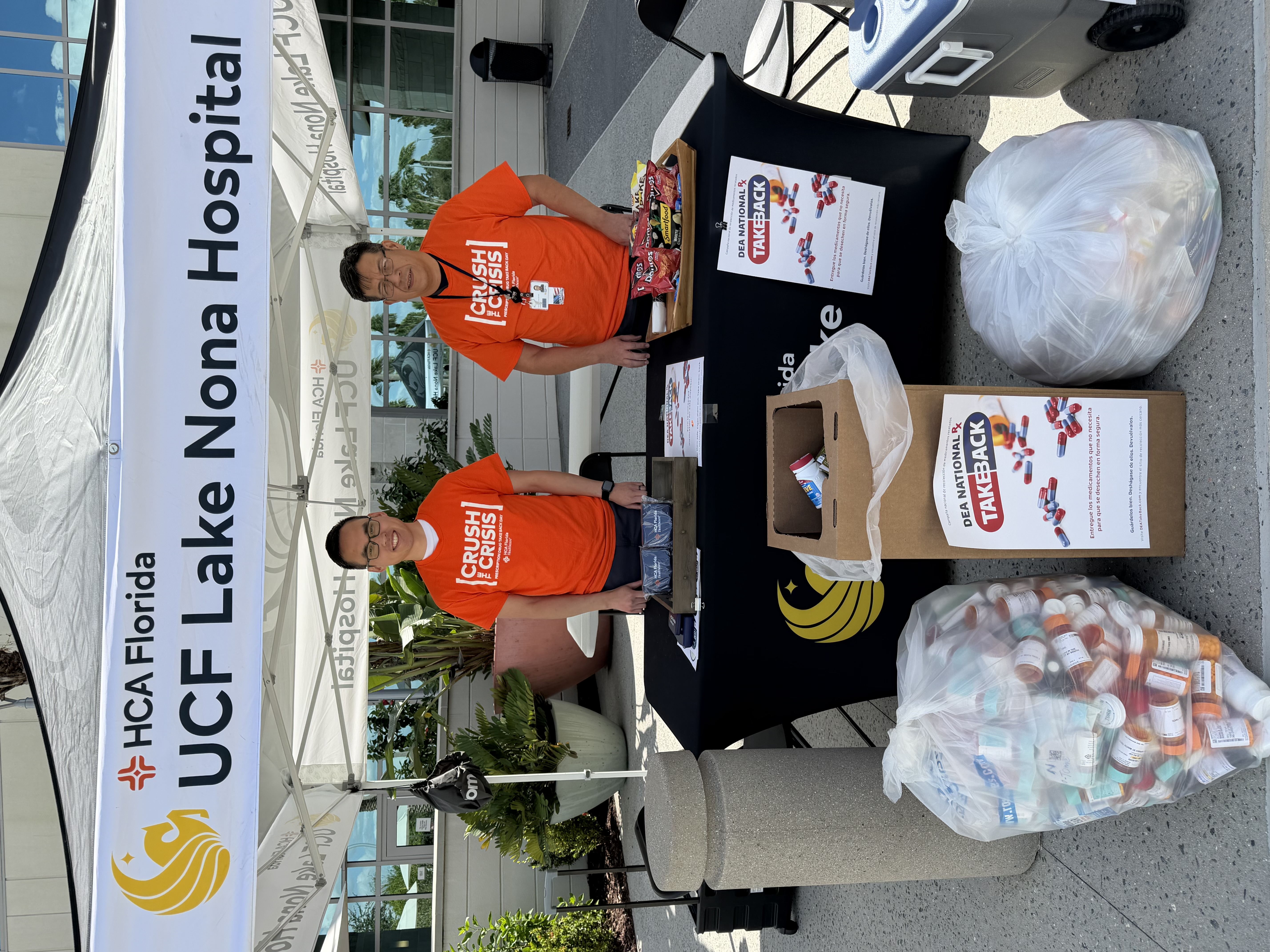 Two volunteers stand under a small tent at a table in front of UCF Lake Nona Hospital.