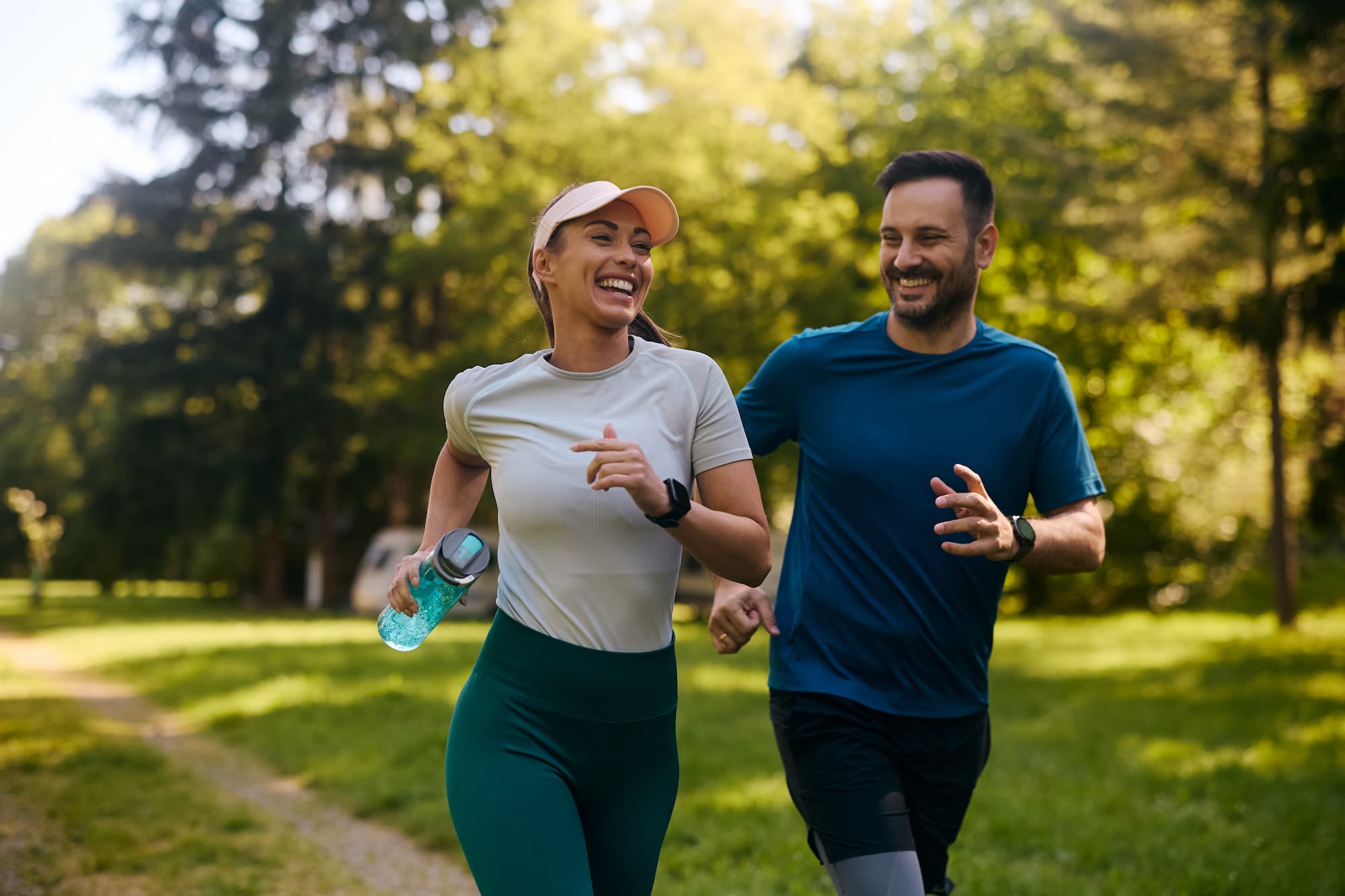 A man and woman smiling while running together in a park.