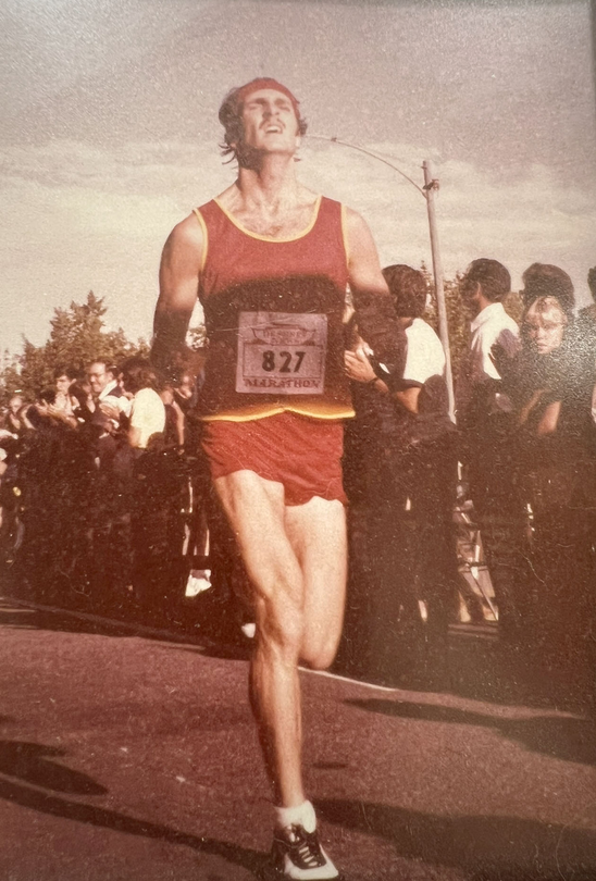 A younger Harold Lance runs in a marathon while spectators watch from the sidelines.