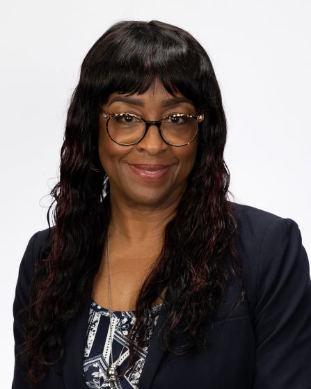 Paulette Woodard with long, wavy hair wearing a dark blazer over a patterned top. 