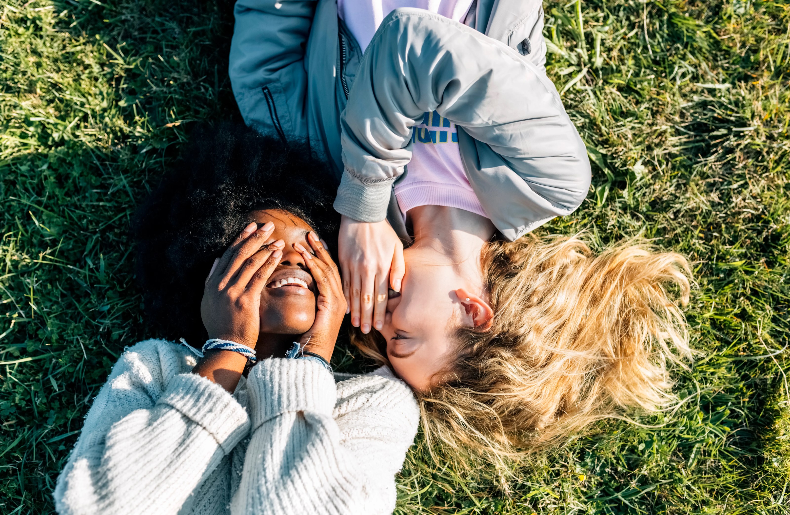 Two women laughing over a secret and laying in the grass.