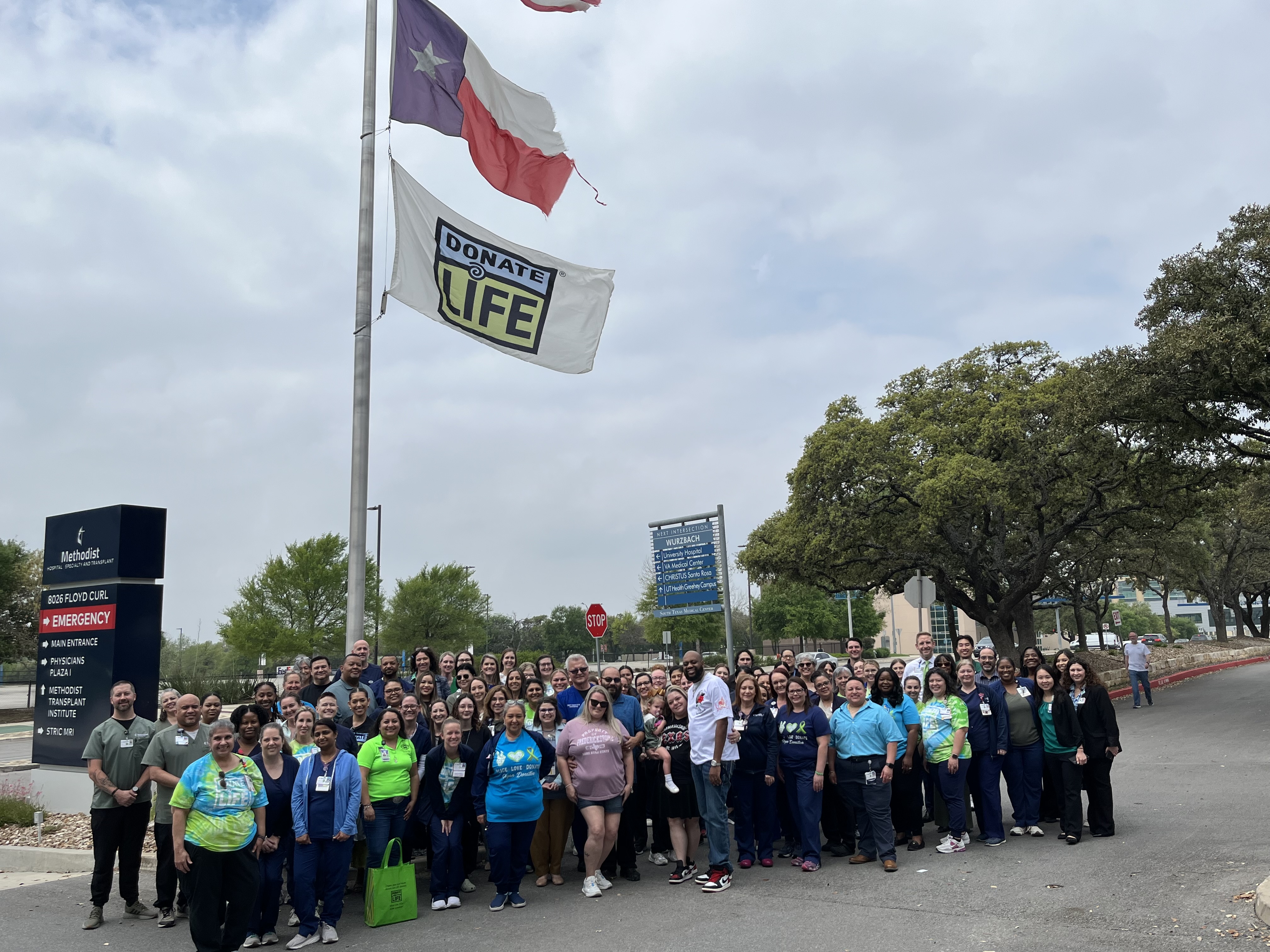 A group of HCA employees standing outside next to a flagstaff outside of the hospital.