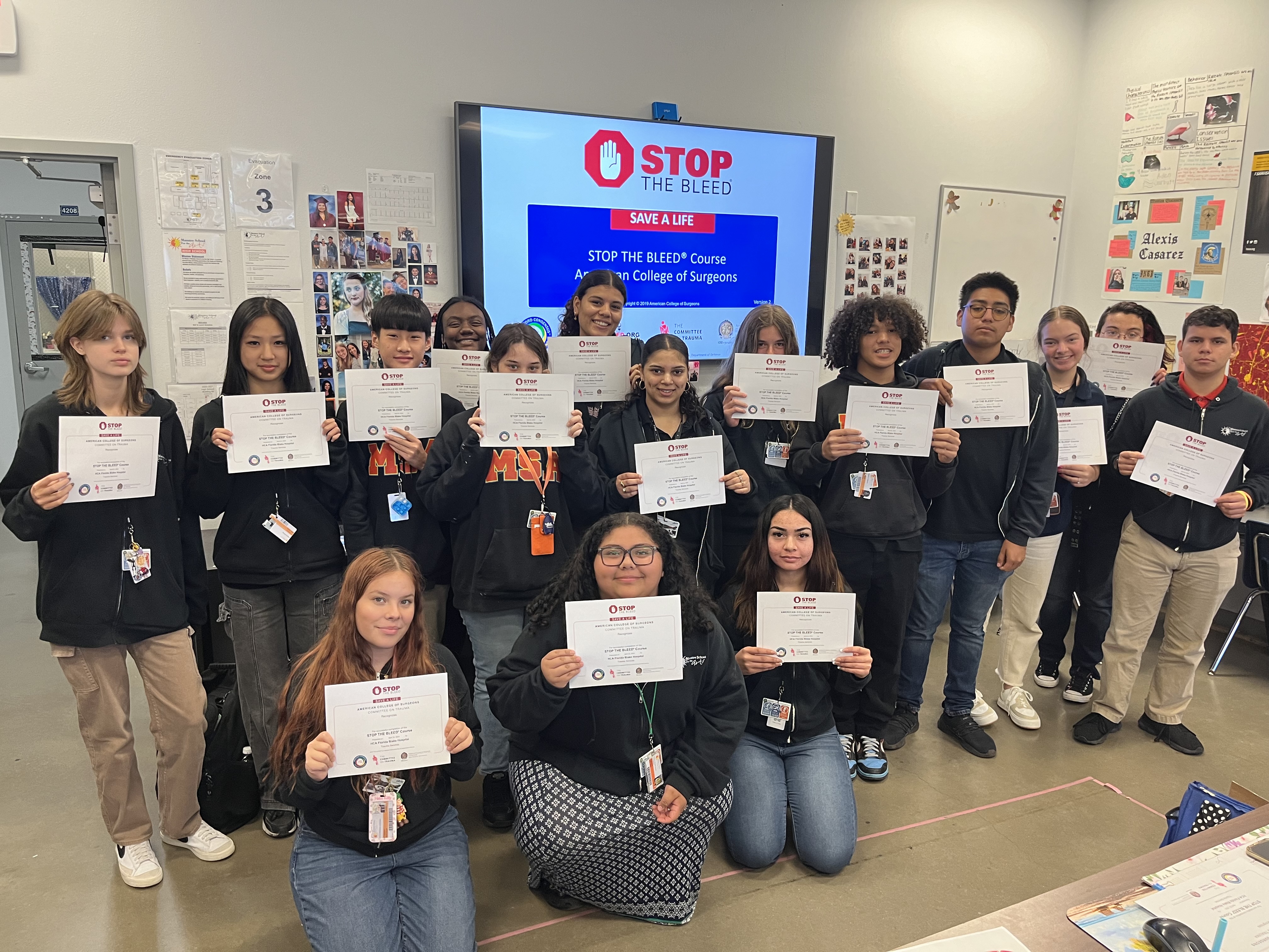 Class of 16 students holding up their "Stop the Bleed" certificates for the camera.