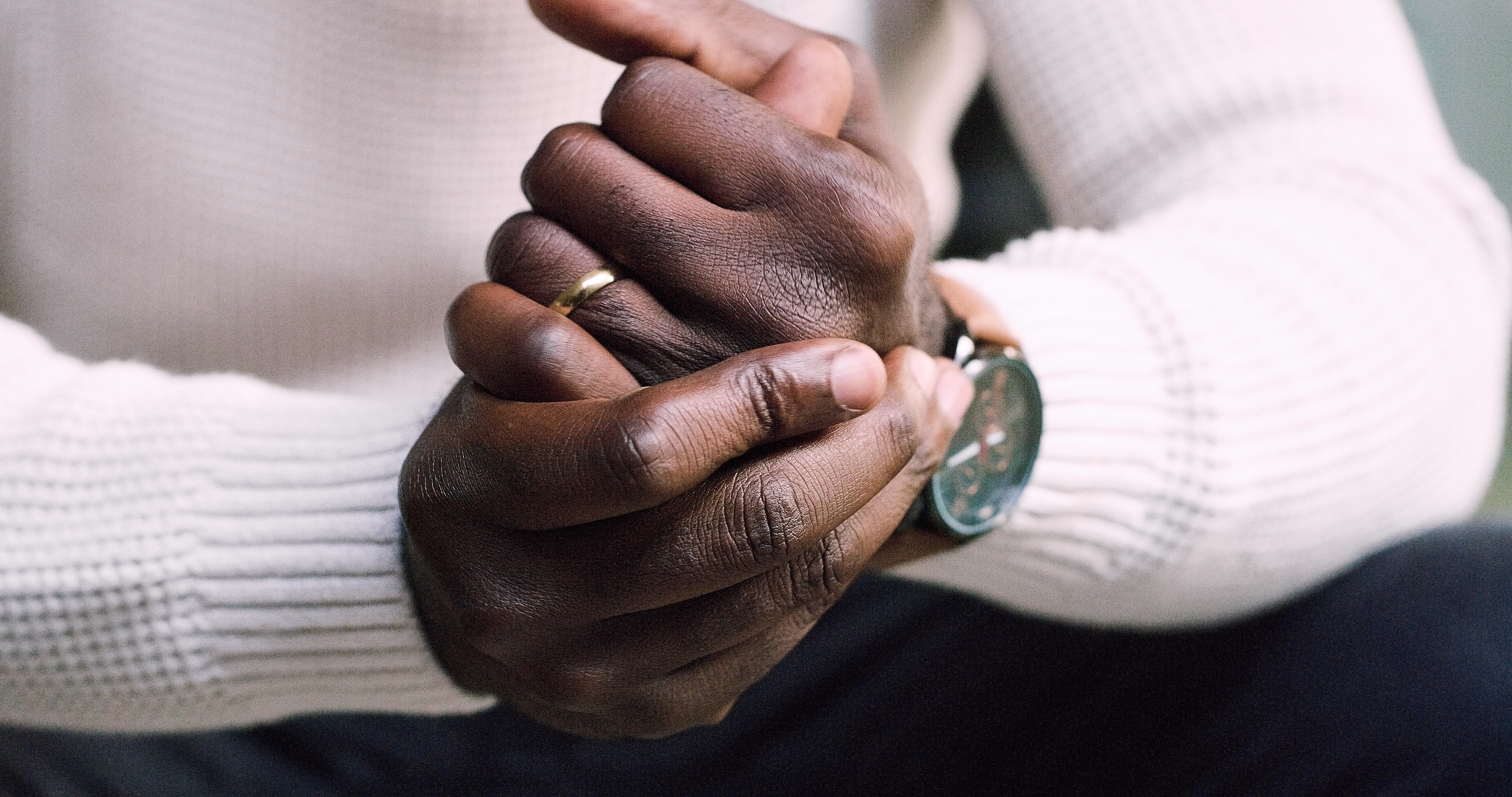A person wearing a ribbed long-sleeve shirt and a watch rubs their hands together.
