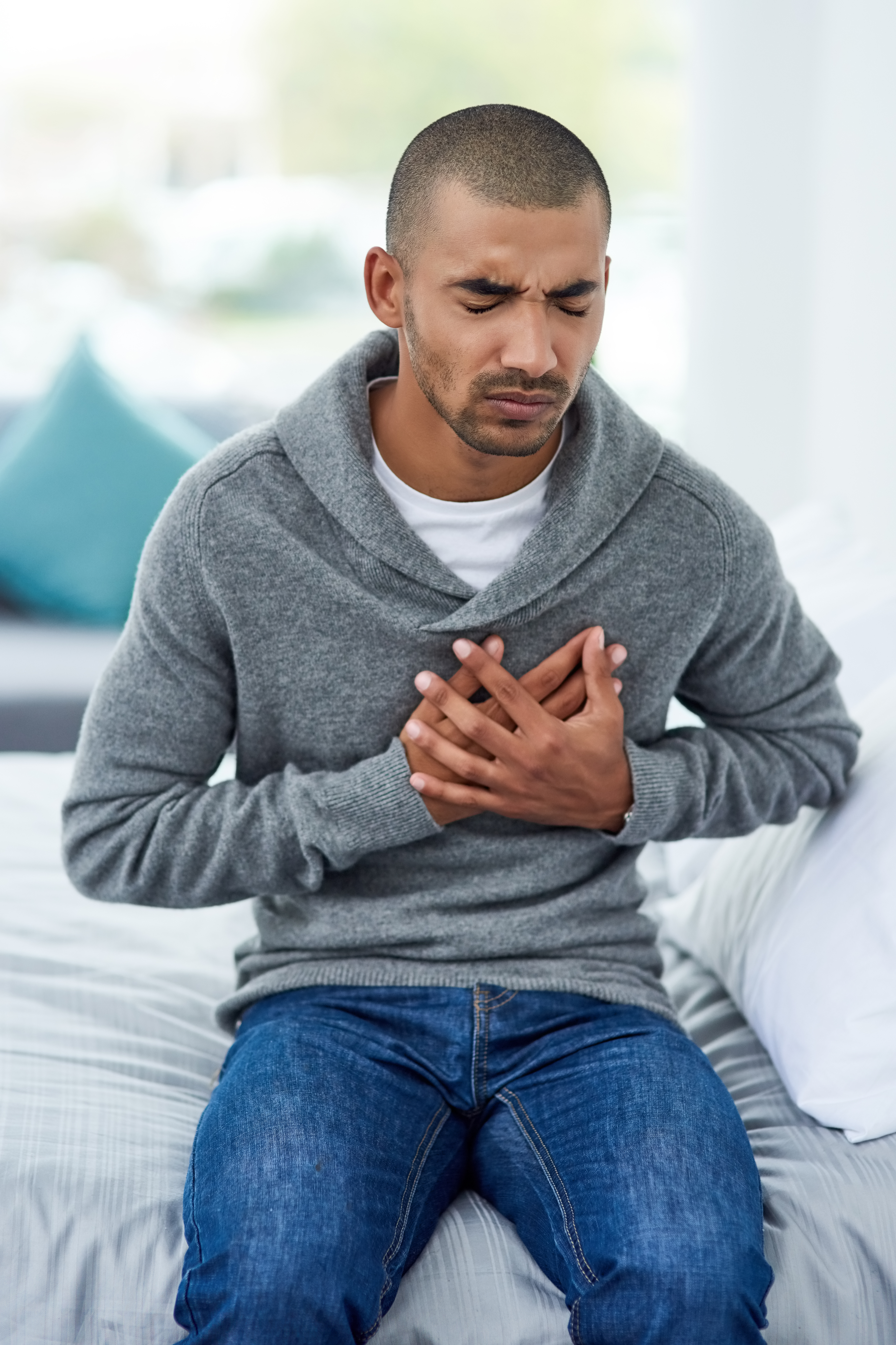 Adult man sitting on bed holding heart with both hands