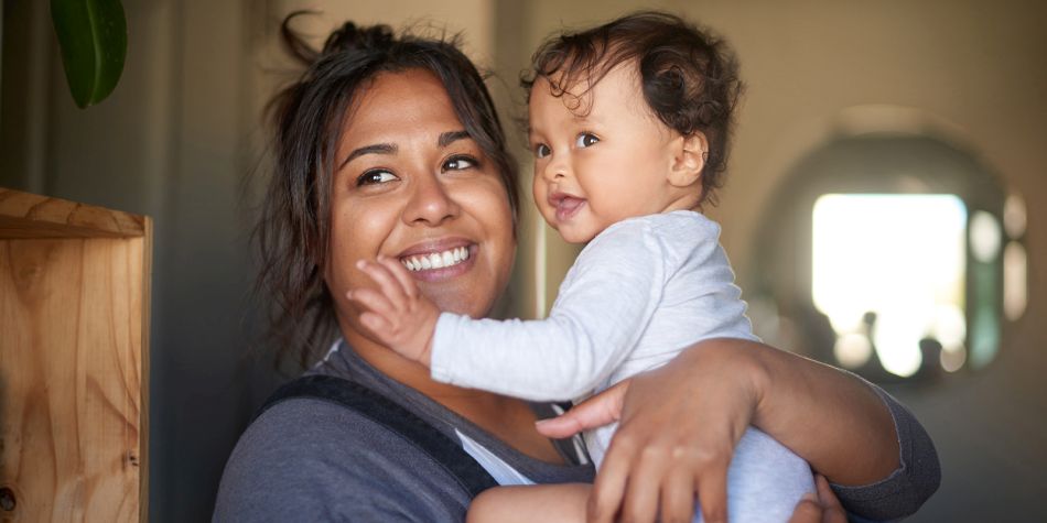 A mom smiling while holding her happy baby.