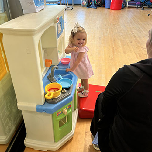 Emma Mansour smiles while playing with a playhouse during a physical therapy session.