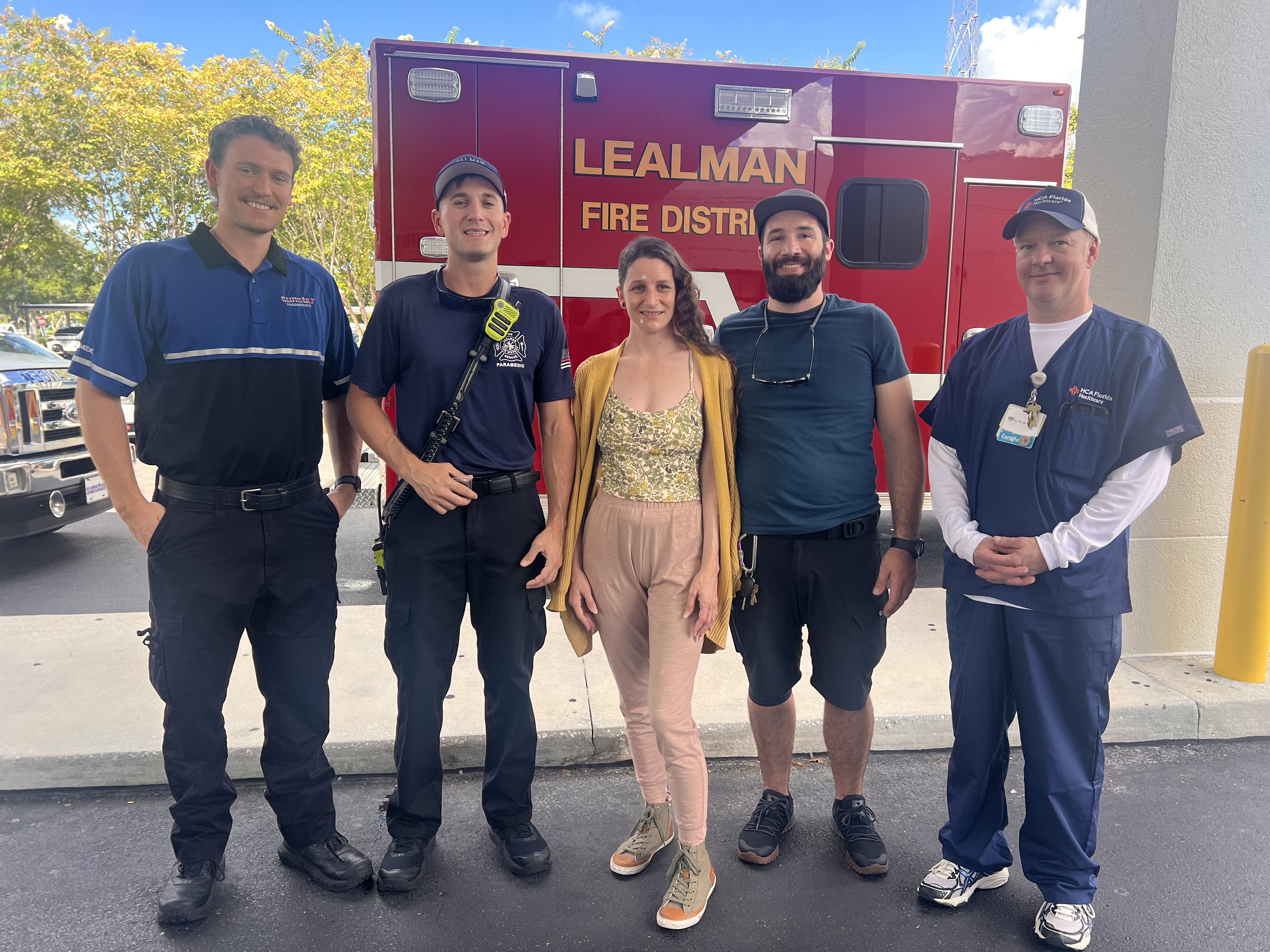 Four EMS crew members pose with a happily recovered Kevyn ZuZu Bartlett in front of an ambulance.