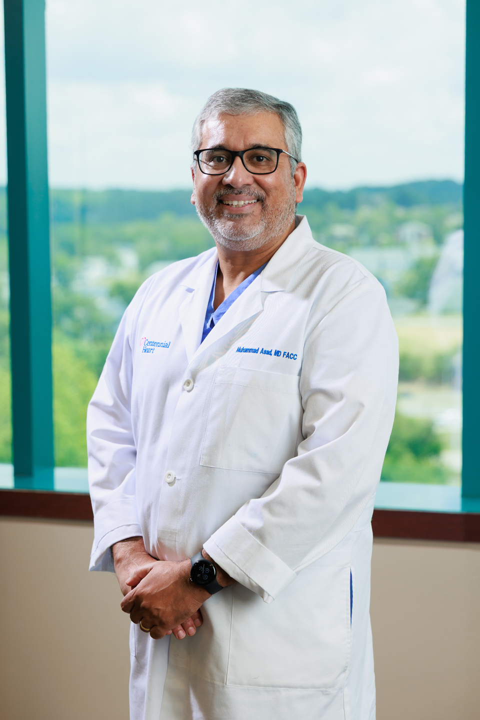 Portrait of a Centennial Heart cardiologist in a white lab coat standing in front of large office windows.