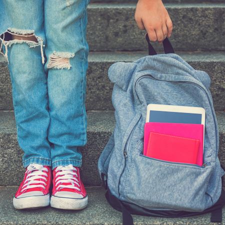 A child holds the handle of a backpack while standing on concrete steps.