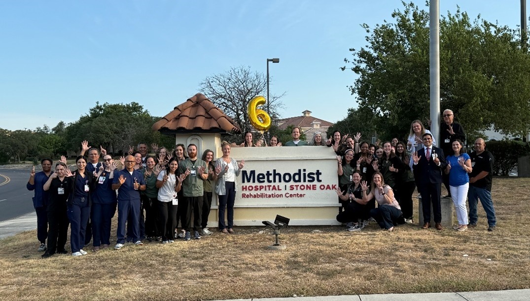 Staff standing in group around Methodist Hospital Stone Oak Rehabilitation Center outdoor sign with gold "6" balloon
