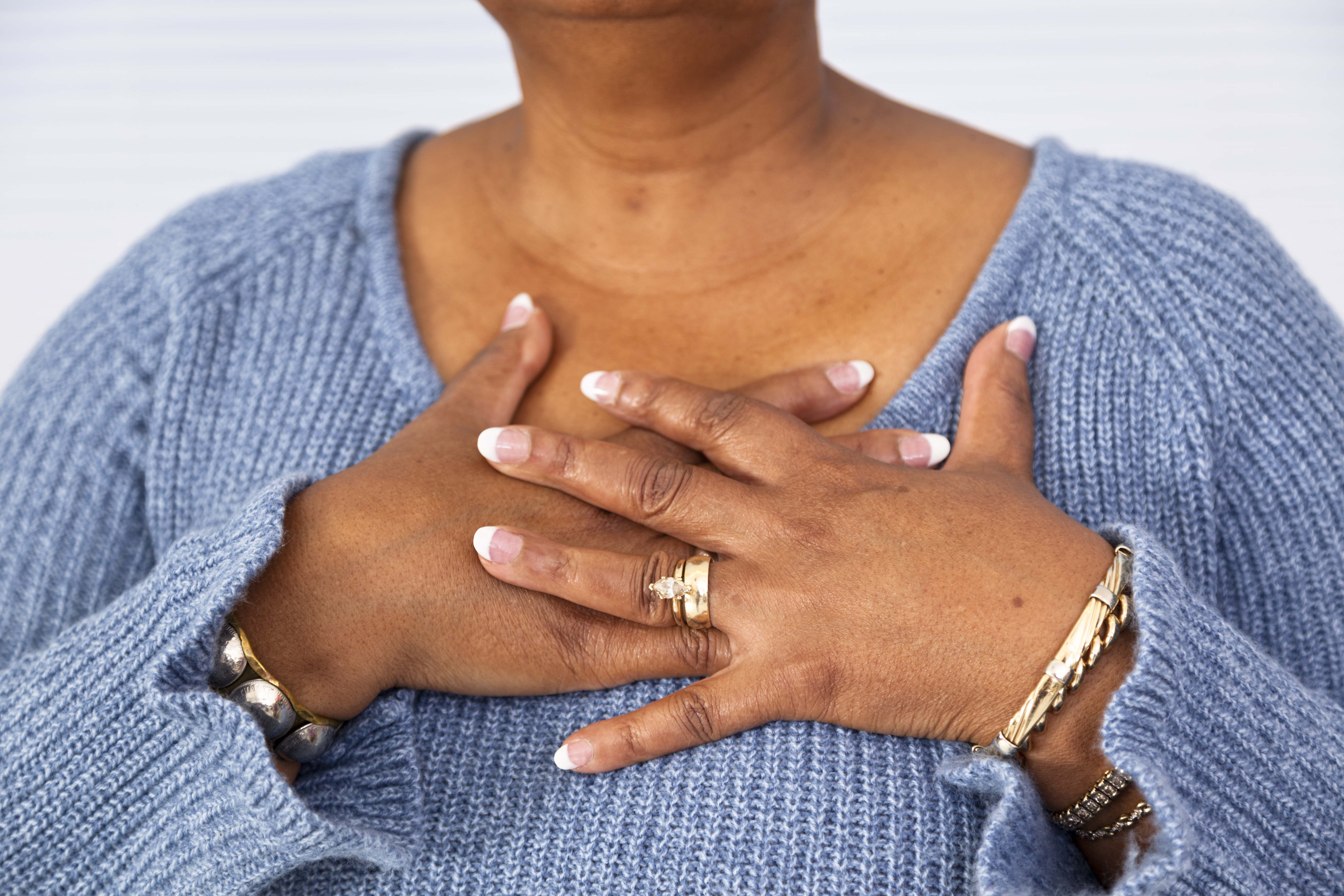 A woman wearing a blue sweater holds both hands over het chest, symbolizing chest discomfort or concern for heart health.
