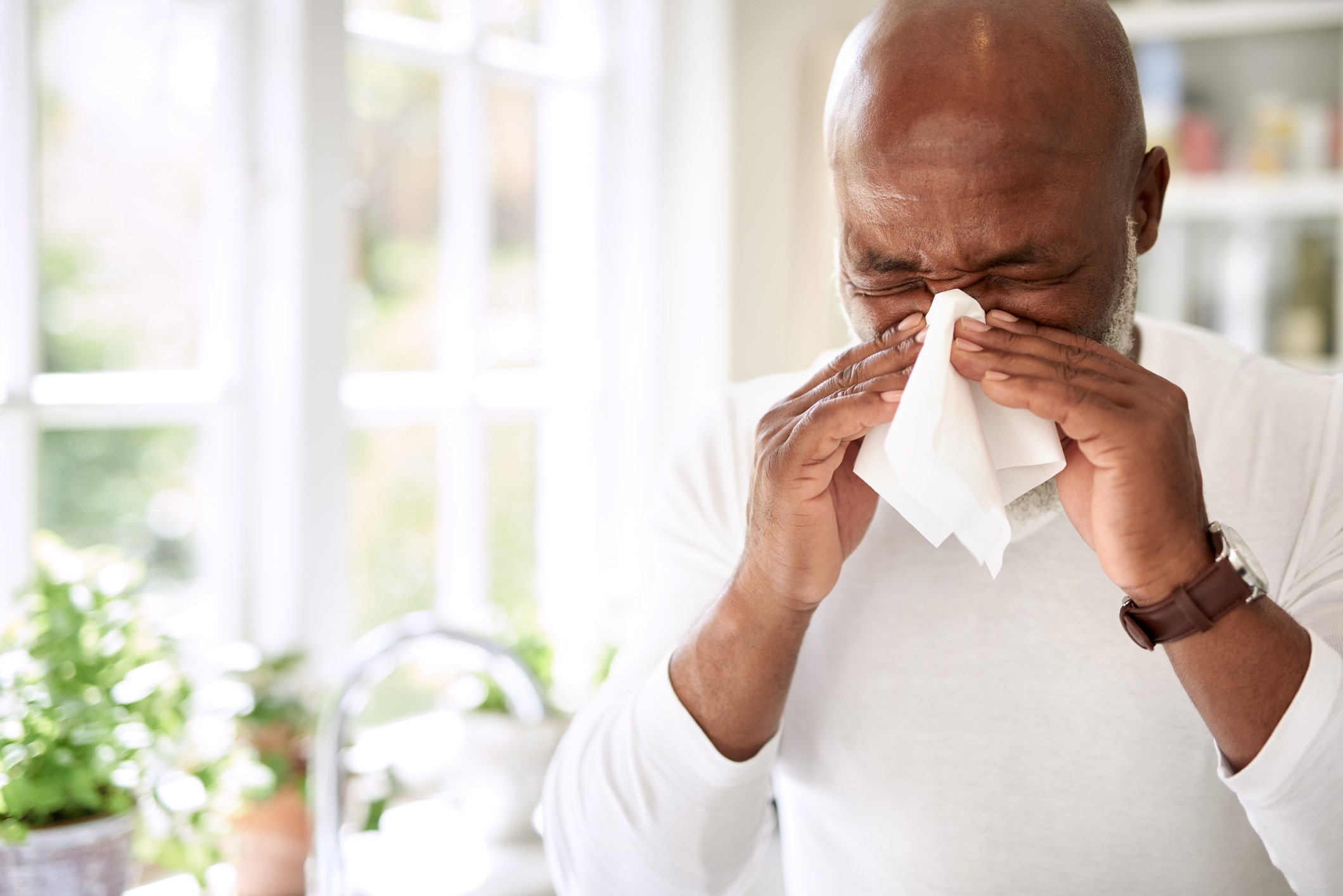 A man blowing his nose with a tissue.